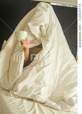 a person wrapped entirely in a blanket, resembling a ghost, holding a coffee cup. High quality photo a person wrapped entirely in a blanket, resembling a ghost, holding a coffee cup. High quality photo 118424774