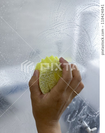 women hand cleaning the shower glass with yellow sponge . High quality photo women hand cleaning the shower glass with yellow sponge . High quality photo 118424841