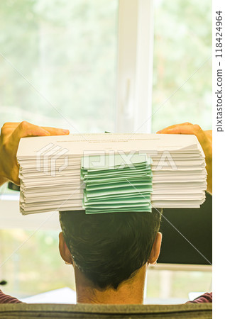 male holds stack of paper on his head in front of window . High quality photo male holds stack of paper on his head in front of window . High quality photo 118424964