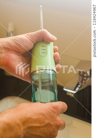male holding the green dental portable water flosser irrigator in bathroom . High quality photo male holding the green dental portable water flosser irrigator in bathroom . High quality photo 118424967
