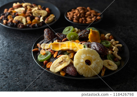 Dried tropical fruits, nuts, and raisins in black plate. Dried tropical fruits, nuts, and raisins in black plate. 118426798