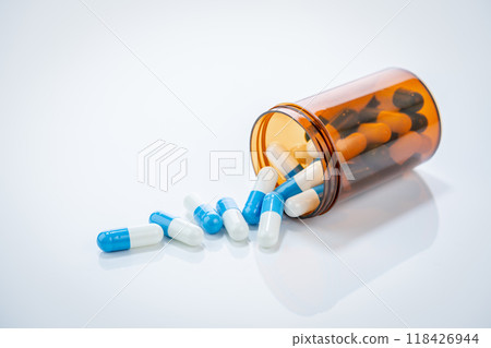 Prescription antibiotic capsules spilling from amber bottle on white background. Blue and white capsule pills. Healthcare and pharmaceutical. Medical treatment pills. Pharmacy and medicine industry. 118426944
