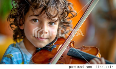 A young boy with curly hair is joyfully playing a violin, a string instrument 118427417