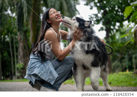 A woman is playing with her dog while taking it for a walk in a park. The dog licks her face. 118428354