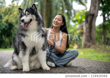 A Siberian husky dog and its Asian female owner are sitting together on a street in a green park. A Siberian husky dog and its Asian female owner are sitting together on a street in a green park. 118428368