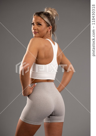 Young woman in workout attire posing confidently in a studio, demonstrating fitness and strength with a focus on active lifestyle and wellness. 118430318