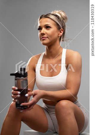 Young woman taking a break from workout with a water bottle in a studio setting, embodying fitness and healthy lifestyle. 118430319