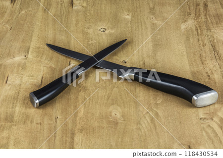 Two metal knives lie on a wooden surface. On the wooden surface lie two metal knives Two metal knives lie on a wooden surface. On the wooden surface lie two metal knives 118430534