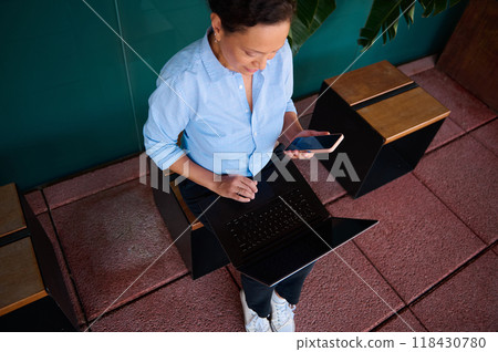 Professional woman multitasking with laptop and smartphone in modern office setting 118430780