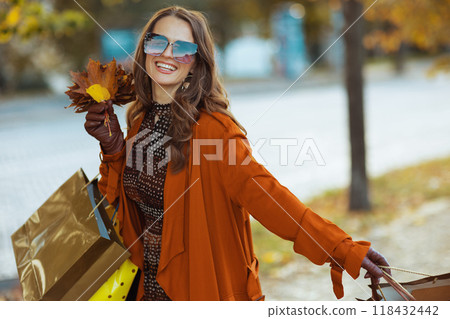 smiling elegant woman in brown trench coat with shopping bags 118432442