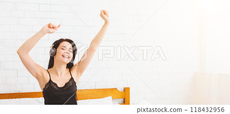 A woman wearing headphones is joyfully lifting her arms up high. She is expressing happiness and excitement through her body language. 118432956