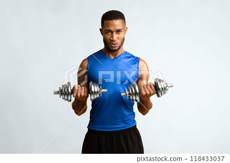 Hard Strength Workout. Determined black bodybuilder exercising with dumbbells over yellow studio wall, copyspace 118433037