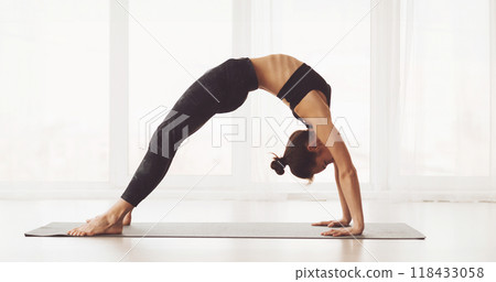A woman is showcased in a spacious, well-lit studio, expertly executing a back-bending yoga pose. She balances on her palms and feet, with her back arched and hips elevated A woman is showcased in a spacious, well-lit studio, expertly executing a back-bending yoga pose. She balances on her palms and feet, with her back arched and hips elevated 118433058