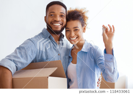 Own Home. Young Afro Spouses Showing New House Key Hugging And Holding Moving Box Standing Indoor. 118433061