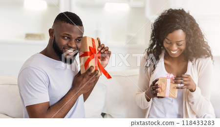 A man smiles and presents a gift to a woman who is opening it with excitement. 118433283