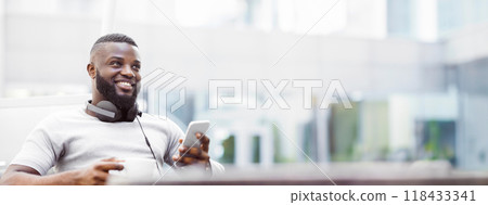 A smiling man sits outside, holding a smartphone and a cup of coffee. 118433341