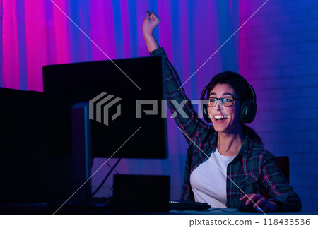 Gamer Young Lady In Headphones Rejoicing when Playing Online Video Games, Sitting In Front Of PC In Neon Room Gamer Young Lady In Headphones Rejoicing when Playing Online Video Games, Sitting In Front Of PC In Neon Room 118433536
