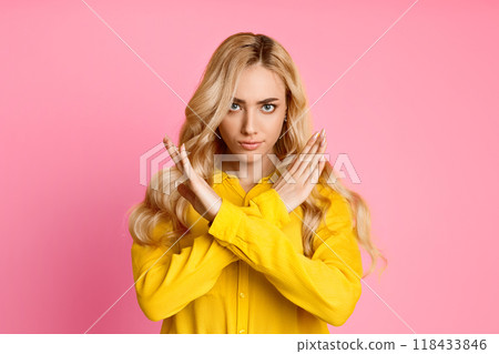 This image shows a blonde woman in a yellow shirt with her arms crossed in front of her, making a no sign. The background is a solid pink color. 118433846