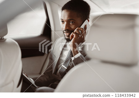 African American man manager in a suit sits in the backseat of a car and talks on his phone. He looks intently at the phone and appears to be engaged in a conversation. 118433942