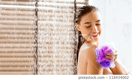 Woman washing with shower gel, standing under water drops and rubbing body with sponge, panorama with copy space 118434002