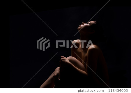 A woman sits with her knees drawn up to her chest, her head tilted back and her eyes closed, copy space 118434003