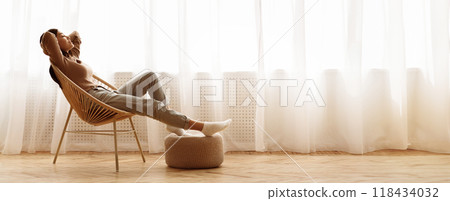 Weekends Finally. Relaxed Girl Sitting on Modern Chair near Window, Enjoying Morning Weekends Finally. Relaxed Girl Sitting on Modern Chair near Window, Enjoying Morning 118434032