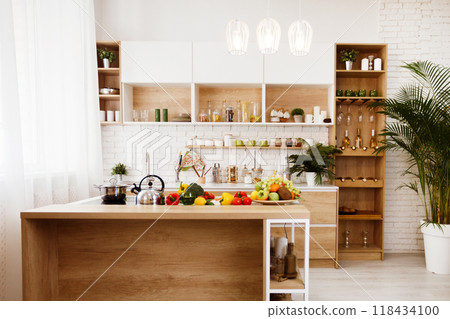 Modern kitchen island with fresh produce on display. The island is made of wood, has a white metal frame. There are several pieces of fruit and vegetables on the counter, including apples, oranges. 118434100