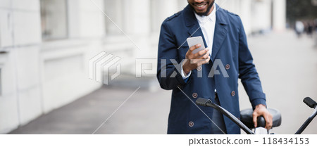 An African American businessman is commuting to his office by bicycle, using his phone. The mood is dynamic and contemporary, emphasizing multitasking and active transportation, cropped An African American businessman is commuting to his office by bicycle, using his phone. The mood is dynamic and contemporary, emphasizing multitasking and active transportation, cropped 118434153