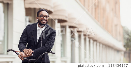 An African American businessman is biking to the office in a bustling city. The setting is dynamic and busy, emphasizing an active and health-conscious lifestyle. 118434157