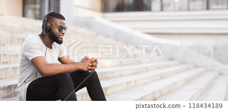 A man wearing headphones and sunglasses sits on a set of stairs, listening to music. 118434189