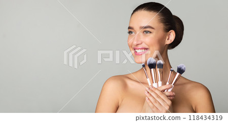 Excited Woman Holding Set of Makeup Brushes, Posing over Grey Background 118434319