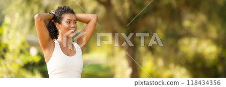 Young woman runner pausing for break in park, smiling and touching hair, exercising contented and healthy outdoors in nature. Fitness and marathon training on summer morning, copy space Young woman runner pausing for break in park, smiling and touching hair, exercising contented and healthy outdoors in nature. Fitness and marathon training on summer morning, copy space 118434356
