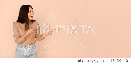 Cheerful Girl Showing Empty Space With Fingers On Peach Studio Background, Panorama 118434440