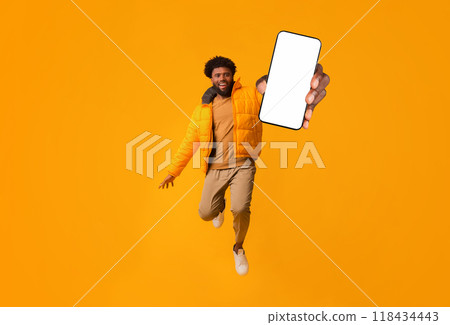Yeah, finally winter sales started. Excited african guy in winter jacket jumping over orange Yeah, finally winter sales started. Excited african guy in winter jacket jumping over orange 118434443