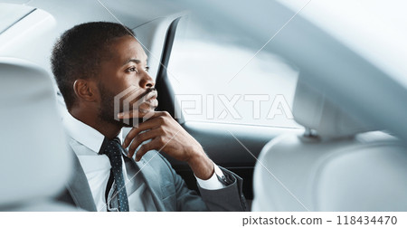 African American businessman in a grey suit, white shirt, and patterned tie sits in the back seat of a car. He is looking out the window and appears to be deep in thought, copy space African American businessman in a grey suit, white shirt, and patterned tie sits in the back seat of a car. He is looking out the window and appears to be deep in thought, copy space 118434470