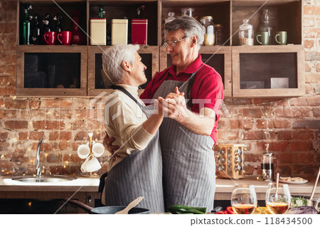 Lovely senior couple dancing and smiling to each other, cooking dinner together in kitchen, empty space 118434500
