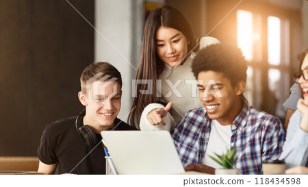 A diverse group of students are gathered around a laptop, attentively looking at the screen. They appear to be engaged in a discussion or viewing content together. A diverse group of students are gathered around a laptop, attentively looking at the screen. They appear to be engaged in a discussion or viewing content together. 118434598
