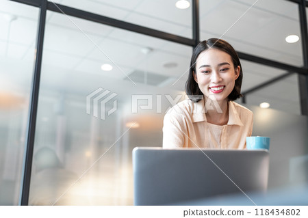 A woman smiling while looking at a computer screen during a break A woman smiling while looking at a computer screen during a break 118434802