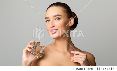 Woman Holding Perfume Bottle and Looking at Camera Over Grey Background 118434812