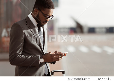 Ordering Taxi. Afro Businessman Using Mobile Phone App, Arriving At Airport, Copy Space Ordering Taxi. Afro Businessman Using Mobile Phone App, Arriving At Airport, Copy Space 118434819