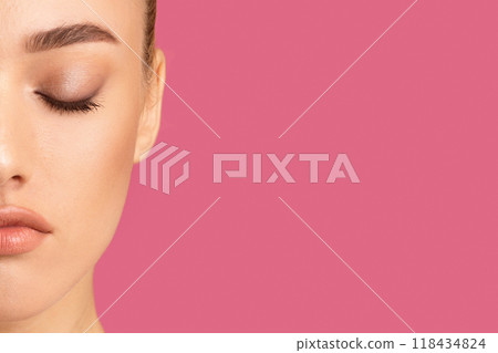 Woman half-face with her eyes closed. The woman face is only partially visible, showing her closed eyes, brow, nose, and lips. The background is a solid, bright pink color, copy space Woman half-face with her eyes closed. The woman face is only partially visible, showing her closed eyes, brow, nose, and lips. The background is a solid, bright pink color, copy space 118434824