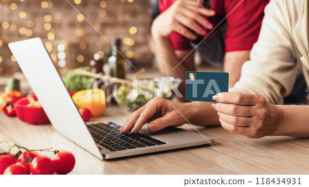 Modern technologies in everyday life. Senior couple using laptop in kitchen for online shopping with credit card, panorama Modern technologies in everyday life. Senior couple using laptop in kitchen for online shopping with credit card, panorama 118434931