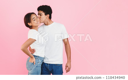 Handsome guy hugging girlfriend and kissing her in cheek over pink background Handsome guy hugging girlfriend and kissing her in cheek over pink background 118434940