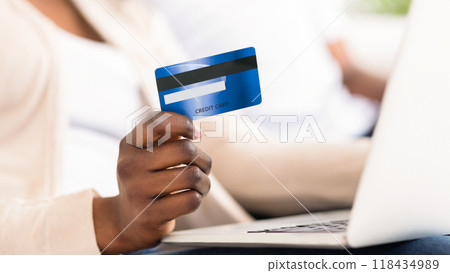 A womans hand holds a blue credit card in front of a laptop, suggesting online shopping or payment. A womans hand holds a blue credit card in front of a laptop, suggesting online shopping or payment. 118434989