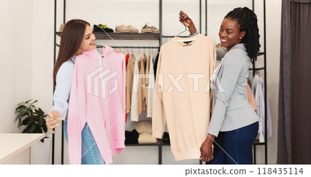 Two multiracial women are standing side by side in fashion store, facing the camera. They are both wearing casual clothing and appear to be engaged in conversation Two multiracial women are standing side by side in fashion store, facing the camera. They are both wearing casual clothing and appear to be engaged in conversation 118435114