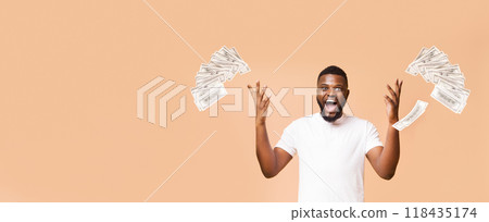 A young African American man wearing a white t-shirt looks excitedly toward the right side of the frame as a large stack of cash flies through the air, surrounded by a soft peach background. 118435174