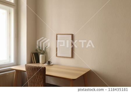 Modern vase with olive branches, old books. Blank vertical wooden picture frame mockup on wall. Home office table near window. Minimal Scandi boho interior. Cup of tea, coffee. Beige wall background. 118435181