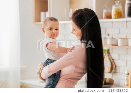 A woman tenderly holds an infant in her arms, cradling the child protectively. The baby looks content and safe in her embrace. A woman tenderly holds an infant in her arms, cradling the child protectively. The baby looks content and safe in her embrace. 118435232