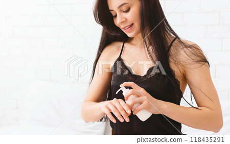 A young woman stands against a light background, gently rubbing her hands together as she applies a moisturizing lotion. Her focus is on ensuring even coverage A young woman stands against a light background, gently rubbing her hands together as she applies a moisturizing lotion. Her focus is on ensuring even coverage 118435291