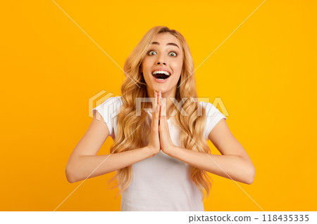A young woman with long, blonde hair is pictured against a yellow background. She is wearing a white t-shirt and has a wide, surprised expression on her face with her mouth open. 118435335